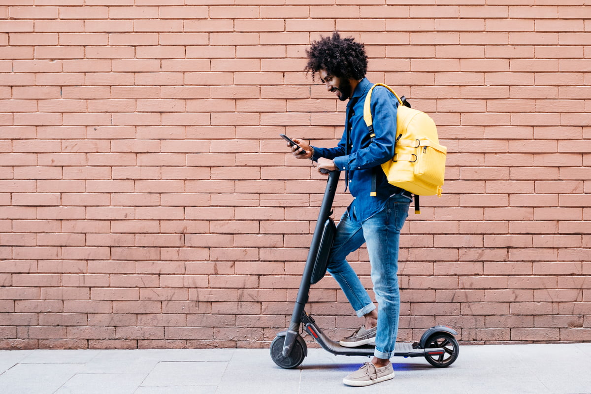 Mann med mobil pa parkert sparkesykkel
