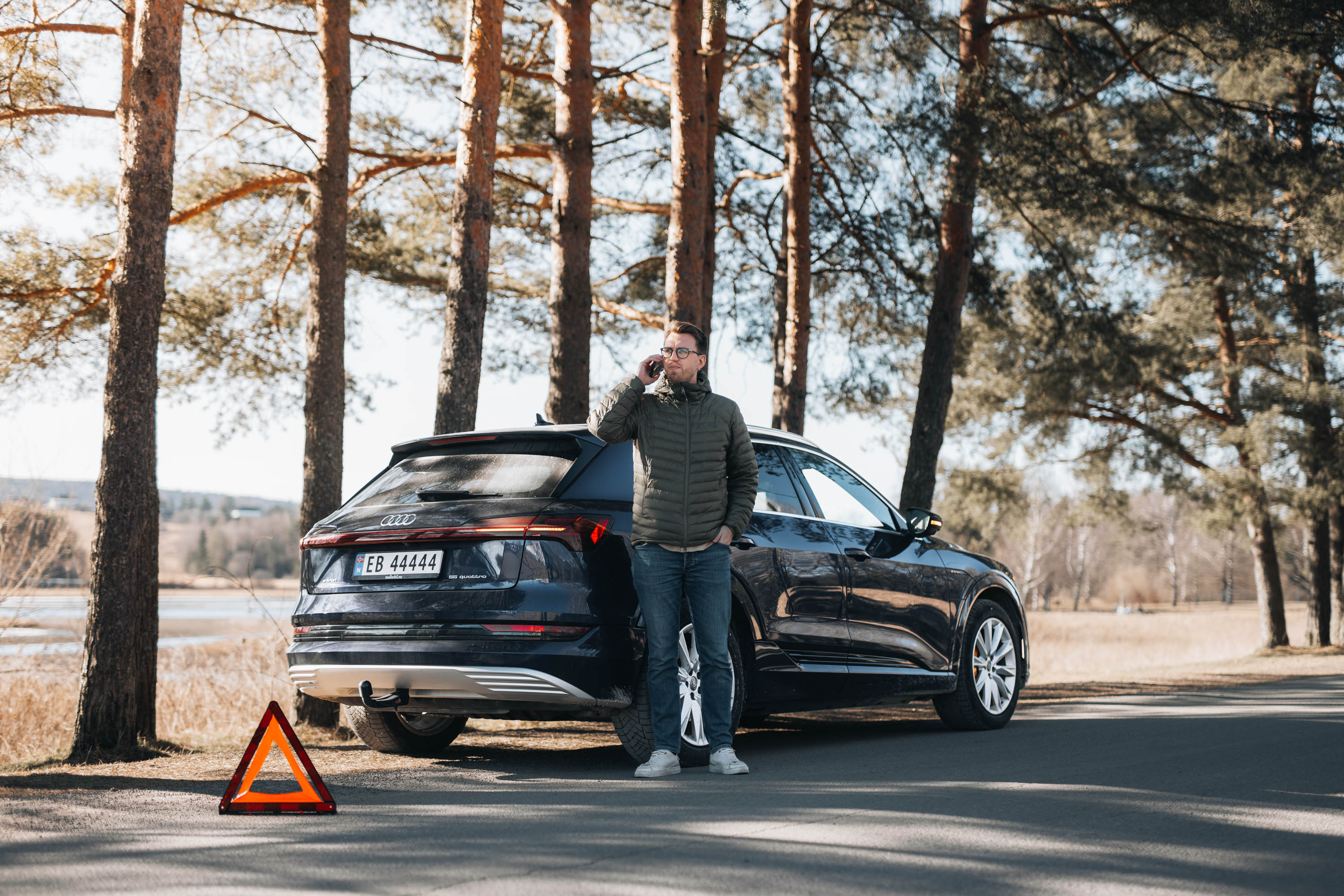 Mann ved bil med motorstopp, snakker i telefon. Varseltrekant plassert bak bilen.